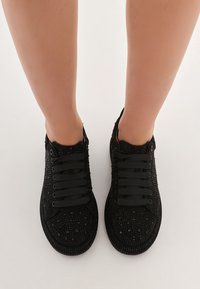 Czarne sneakersy na sznurówki z teksturowaną powierzchnią i wypukłymi ozdobami. Okrągły czubek, gumowa podeszwa i płaskie czarne sznurowadła.