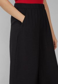 Zwarte wijde broek met een textuur, voorzien van een elastische tailleband en zijzakken, weergegeven tegen een neutrale achtergrond.