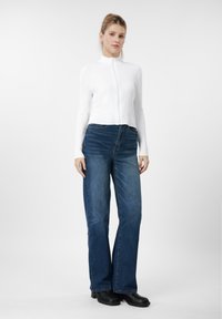 Camisola branca com fecho de correr e padrão em relevo, jeans azul de cintura alta com pernas largas, botas pretas robustas; textura lisa, linhas direitas, desgaste subtil nos jeans.