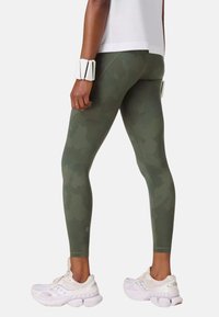 Leggings met een groen camouflagepatroon en een gladde textuur, een ontwerp met hoge taille, gecombineerd met witte sportschoenen en een wit polsbandje.