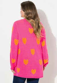 Gorący różowy sweter z pomarańczowymi wzorami serc, z długimi rękawami i luźnym krojem, wykonany z miękkiego, strukturalnego materiału dzianinowego.