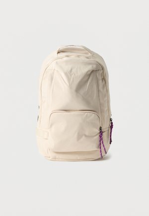 Zaino beige con tasca frontale con cerniera e cordini viola per la zip, mostrato in posizione verticale su sfondo bianco semplice.