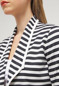 Giacca a righe con sottili strisce bianche e blu navy. Presenta un colletto a scialle e un tessuto morbido e liscio in misto cotone.