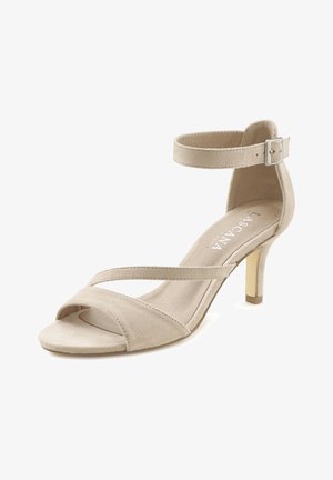 Beige Wildleder-Pumps mit überkreuzten Riemen und verstellbarem Knöchelriemen. Verfügt über einen moderaten Blockabsatz und eine weiche, strukturierte Oberfläche.