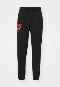 Pantalones de chándal negros con cinturilla elástica y cordón ajustable. Presentan el logo en rojo "CHICAGO BULLS" y un gráfico de un toro en el muslo izquierdo.