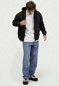 Hoodie preto com fecho, camisa branca texturizada por baixo, jeans azuis de perna reta e sapatos pretos com detalhes claros.