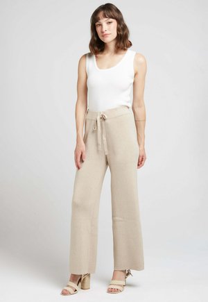 Pantalons larges beige à côtes avec un détail à cordon, associés à un haut sans manches blanc et des sandales à talons blocs de couleur claire.