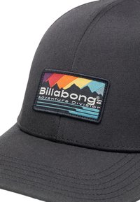 Svart caps med buet skjerm og teksturert stoff; har et flerfarget fjelllogo-patch med teksten "Billabong Adventure Division".