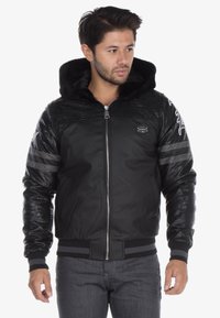 Black bomber jacket with a faux fur hood; textured mesh and smooth leather panels; includes striped accents on the sleeves and zip closure.