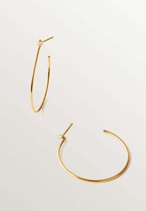 Pendientes de aro delgados de oro con pequeños sujetadores traslúcidos, descansando sobre una superficie clara, uno de pie y el otro acostado.