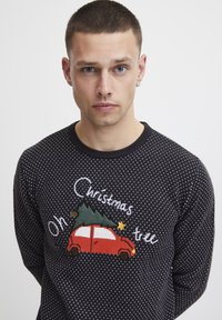Maglione nero con pois bianchi, con un design ricamato di un'auto rossa che trasporta un albero di Natale e la scritta "Oh albero di Natale."