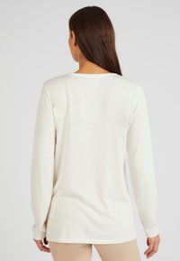Langarmshirt van zacht crèmekleurig stof, met een relaxte pasvorm en ronde halslijn. De achterkant is glad met een lichte draping en zonder verdere versieringen.