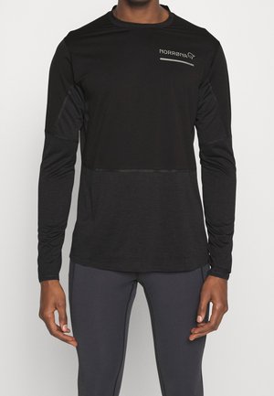 Mężczyzna ubrany w czarną długorękawową sportową koszulkę z logo "Norrøna" na piersi oraz ciemnoszare dopasowane sportowe spodnie.