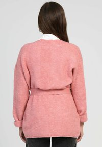 Cardigan en laine rose clair avec une taille ceinturée, design ouvert, manches larges et accents côtelés aux poignets et à l'ourlet. Texture douce.