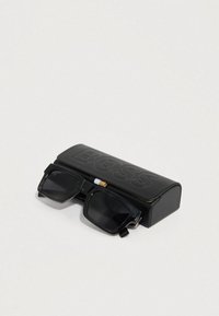 Óculos de sol pretos com armação quadrada repousando sobre um estojo preto gravado com "BOSS." O estojo tem uma textura suave e design curvo.