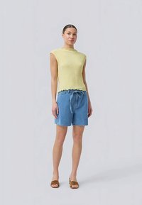 Kollane ribaga kudumata ilma varrukateta topp, millel on laineline serv, koos helesinise denimist lühikeste pükste ja elastse vöökohaga, millel on string. Pruunid sussid.