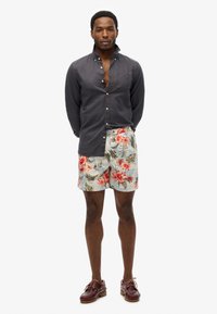 Donkere overhemd met knoopjes gecombineerd met lichte bloemenhortensia met rode en groene patronen, aangevuld met donkerbruine schoenen.