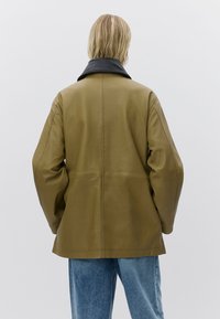 Bruine leren jas met een zwarte kraag, met een ontspannen pasvorm, zichtbare naden en een gladde textuur. Draagt op lichtblauwe spijkerbroek.