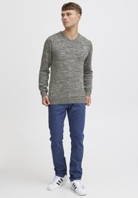 Maglione grigio a maglia testurizzata con scollo a V e orlo a coste abbinato a pantaloni blu e sneakers bianche con strisce nere.