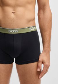 Fekete boxer alsónadrág zöld elasztikus derékpánttal, amelyen fehér betűkkel szerepel a "BOSS" felirat. Simaságot adó anyag, amely szorosan illeszkedik.