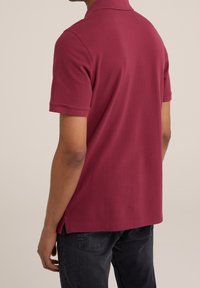 Vínově červený polo tričko s krátkými rukávy, límečkem a bočními rozparky. Materiál má hladkou strukturu, vhodný pro volnočasové nošení.