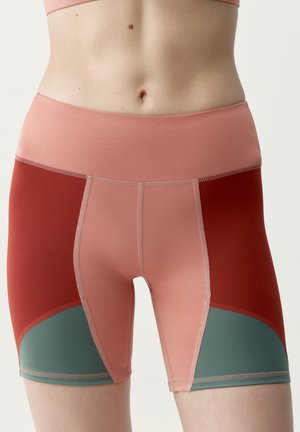 Nahaufnahme einer Person, die hoch taillierte, farblich abgesetzte Sportshorts in Rosa-, Rot- und Grüntönen vor einem schlichten Hintergrund trägt.