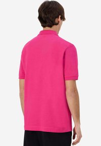 Polo shirt in cotone rosa con maniche corte, colletto e texture liscia. Presenta un orlo dritto e nessun logo o motivo visibile.
