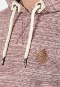 Bluza z kapturem w kolorze wina w melanżowanym materiale, z kremowymi sznurkami do ściągania, metalowymi oczkami oraz kwadratową skórzaną naszywką z wytłoczonym logo.