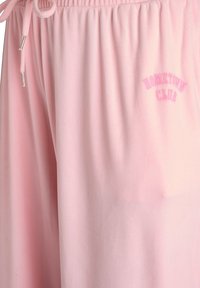 Lyserøde joggingbukser lavet af blødt stof, med en elastisk talje med snører og en lille broderet "HOMETOWN CLUB"-logo.