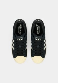 Μαύρα υφασμάτινα αθλητικά παπούτσια με λευκές ρίγες και λαστιχένιο κάλυμμα μύτης. Διαθέτουν μαύρα κορδόνια και λογότυπο στη γλώσσα και στο πλάι.