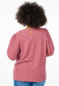 Blouse rose chiné avec manches bouffantes, texture florale, détail en forme de trou de serrure au dos et encolure arrondie, associée à un bas en denim bleu.