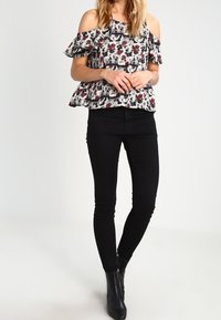 Haut floral à épaules dénudées avec manches à volants en noir, blanc et rouge, associé à un jean noir ajusté et des bottines.