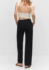 Jeans negros de pierna ancha con cintura alta, combinados con un crop top ceñido de punto color crema que presenta bordes en forma de concha y detalle en la parte posterior abierta.