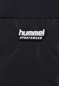 Schwarzer Stoff mit einer glatten Textur, der ein erhabenes weißes Logo zeigt, das in fetten Buchstaben "hummel SPORTSWEAR" liest.