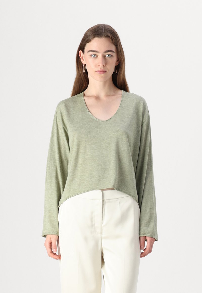 Långärmad ljusgrön topp med V-hals, med en avslappnad passform och en cropped fåll. Mjuk textur med minimalistisk design. Matchas med vita byxor.