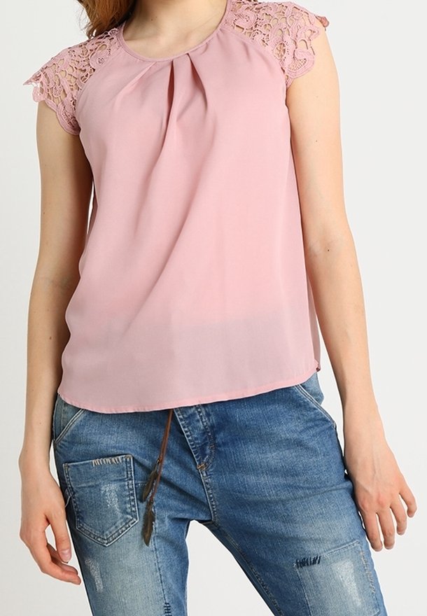 Blusa rosa con maniche in pizzo, davanti plissettato e texture morbida. Abbinata a jeans in denim blu scoloriti.