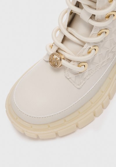 Sneaker alta di colore crema con pelle e tessuto a motivo. Presenta occhielli dorati, lacci e un'emblematic logo. Design con suola spessa.