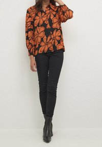 Blusa nera con grande motivo floreale arancione, con bottoni sul davanti, colletto e maniche lunghe. Abbinata a jeans skinny neri e stivaletti.