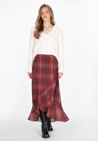 Maglione a maglia crema con scollo a V, abbinato a una gonna a quadri rossa con orlo arricciato e stivali neri al ginocchio.