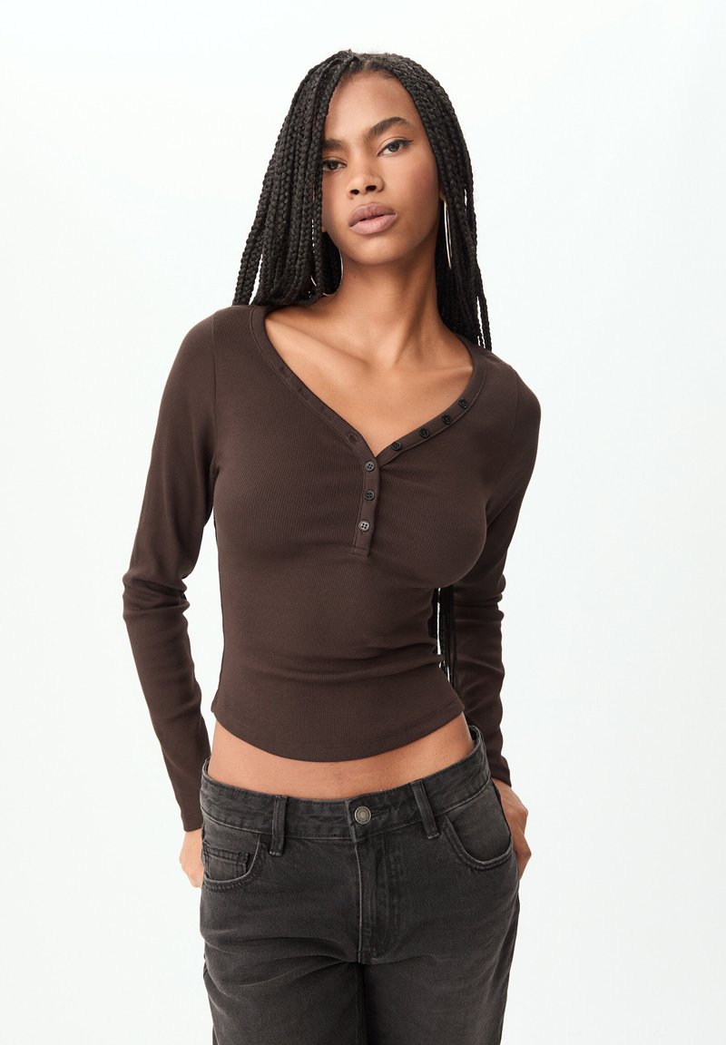 Haut long à rayures brun avec un col en V et une patte de boutonnage, associé à un jean noir taille haute. Texture lisse, design ajusté.