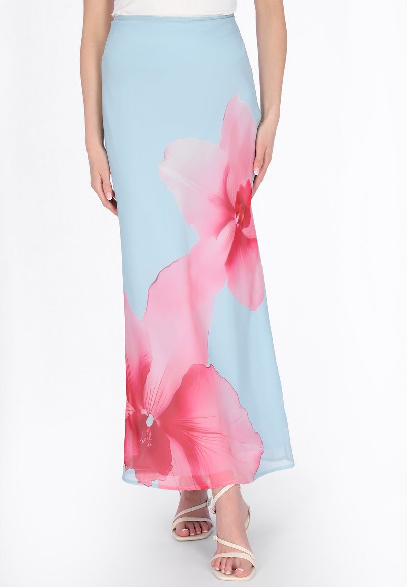 Hellblauer Maxirock mit großem pinkfarbenem Blumenmuster, kombiniert mit weißen Riemchensandalen und einem weißen Oberteil, gezeigt von der Taille bis zu den Füßen.