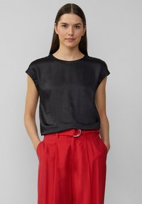Haut noir à manches courtes en tissu lisse, avec un col rond et une coupe décontractée. Associé à un pantalon rouge taille haute.