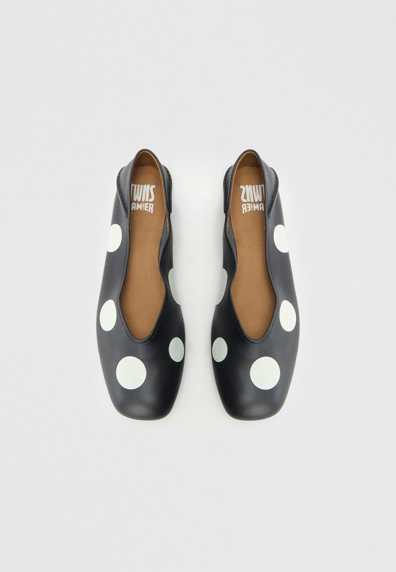 Sorte flade sko med store hvide polkaprikker. Glat, mat tekstur, udskårne sider og en rundet tå. Brun lædersål.