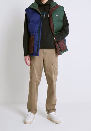 Färgglad puffväst i blått, grönt och vinrött, bärs över en svart hoodie, kombinerad med beige cargobyxor och vita sneakers.