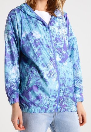 Lekka kurtka zapinana na zamek z kapturem, z niebiesko-fioletowym wzorem tie-dye, elastycznymi mankietami i kieszeniami bocznymi. Gładka tekstura.