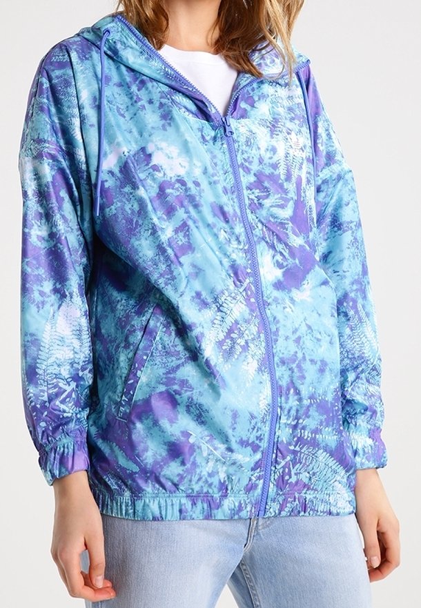 Lightweight zippered jacket with a hood, featuring a blue and purple tie-dye pattern, elastic cuffs, and side pockets. Smooth texture.