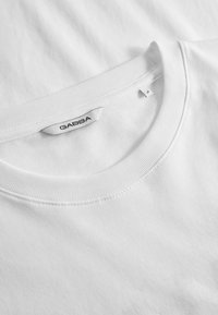 Tricou alb din bumbac cu guler rotund ribbed și un eticheta GABBA cusută în zona gâtului; textură moale, design simplu și fără modele.