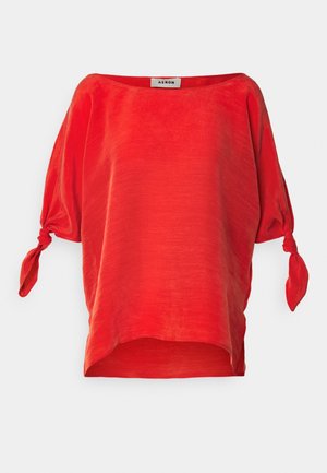 Top in lino rosso con scollatura ampia, maniche a sbuffo fissate con nastri e vestibilità morbida. Texture liscia e lucentezza distintiva.