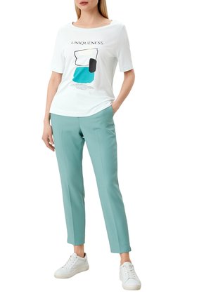 T-shirt graphique blanche avec le texte "UNIQUIDÉ" et des accents turquoise, à manches courtes, associé à un pantalon bleu clair et des baskets blanches.