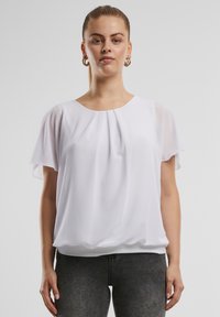 Top bianco a maniche corte con design plissettato, tessuto morbido, scollatura rotonda e vestibilità rilassata, abbinato a jeans scuri. Leggero e fluido.